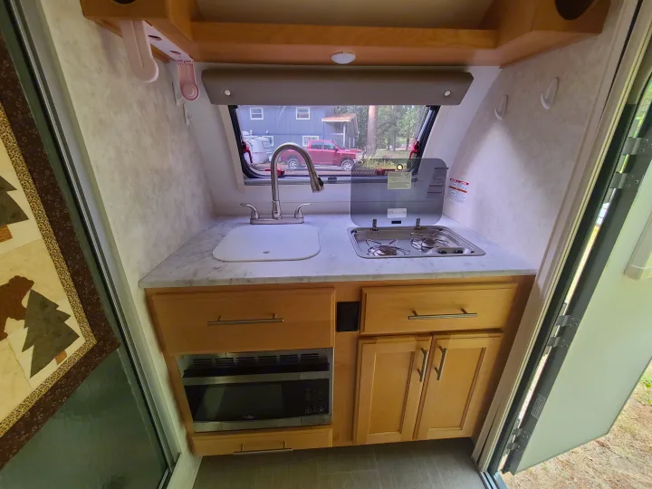 Compact RV rental kitchen: sink, stove, microwave, and wooden cabinets provide all necessities for on-the-road cooking.. Xtreme Outdoors Little Guy 2019