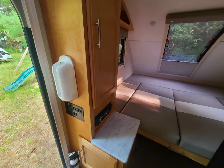 Inside an RV rental: Compact living space with convertible bed, system controls, and outdoor view through the door.. Xtreme Outdoors Little Guy 2019