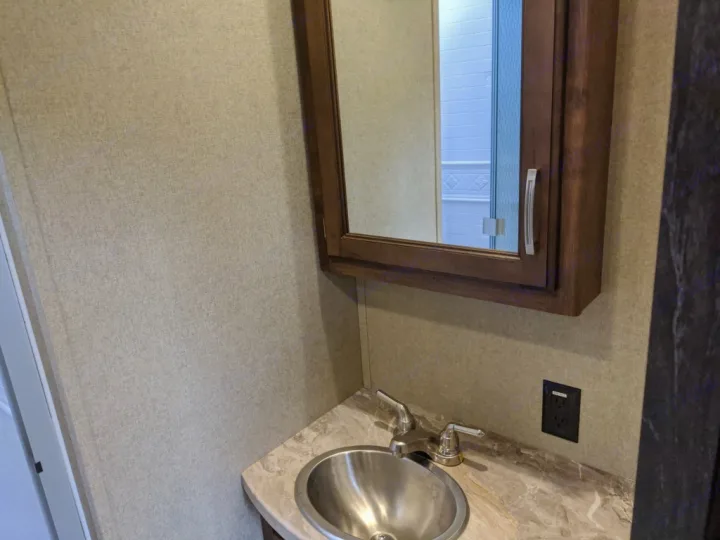 Compact RV rental bathroom with a silver sink, mirrored medicine cabinet, and electrical outlet above a marble-look vanity.. Grand Design Reflection 2018