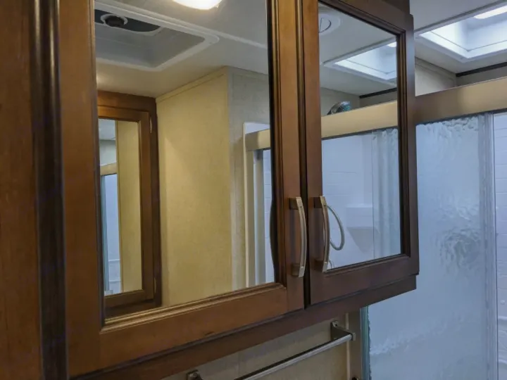 Mirrored cabinets in an RV rental bathroom reflect a clear/frosted glass shower stall and ceiling vent.. Grand Design Reflection 2018