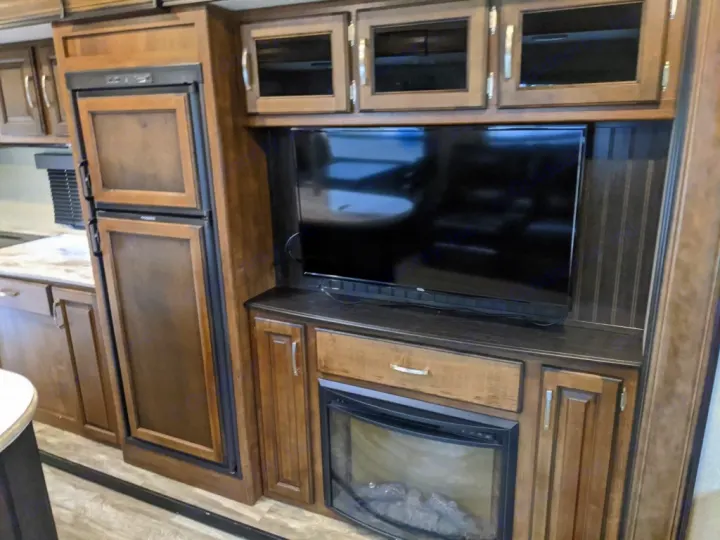 RV rental interior featuring modern wood cabinets, built-in fridge, TV, and an electric fireplace for cozy travel.. Grand Design Reflection 2018