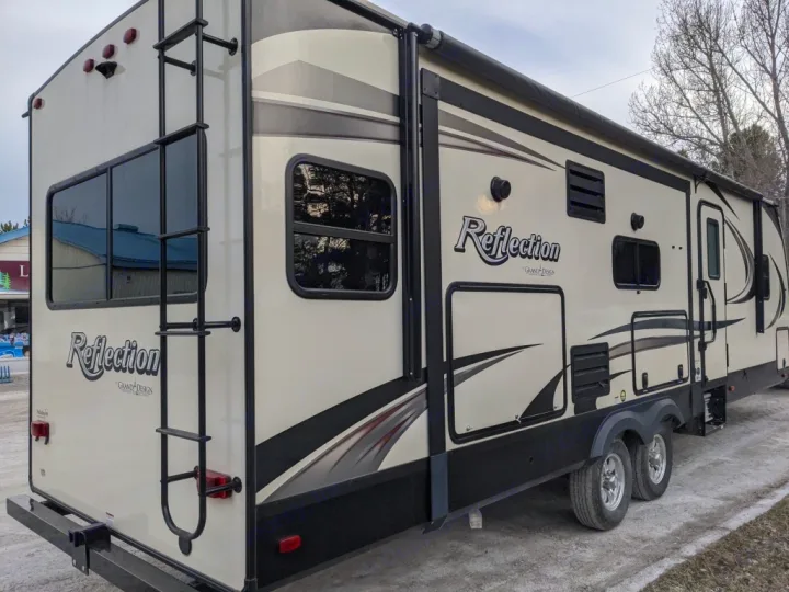 This beige Grand Design Reflection travel trailer, perfect for an rv rental, features a rear ladder, side awning, and dual axles.. Grand Design Reflection 2018