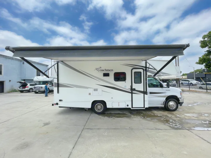 A white Coachmen Freelander RV rental motorhome with extended awning on a paved lot. Cloudy sky above.. Coachmen Freelander 2021