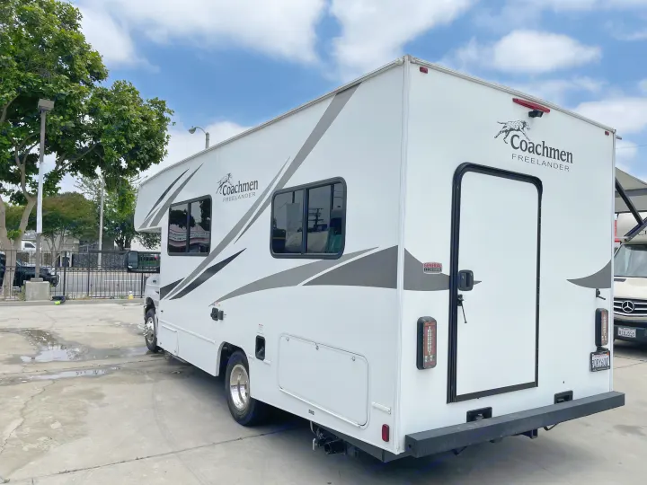 White Coachmen Freelander Class C RV rental parked outdoors, showcasing its side and rear with graphics.. Coachmen Freelander 2021