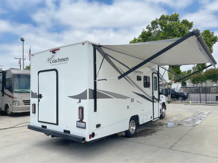 White Coachmen Freelander Class C motorhome (rv rental) with extended awning, viewed from rear, parked on a concrete lot.. Coachmen Freelander 2021