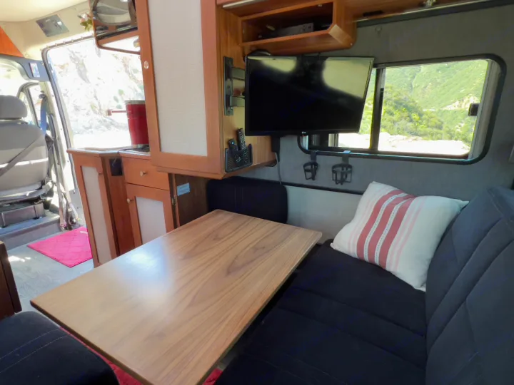 Spacious RV rental interior: cozy seating, table, kitchen, TV, and mountain views from the window. Perfect for van life.. Roadtrek Simplicity SRT 2019
