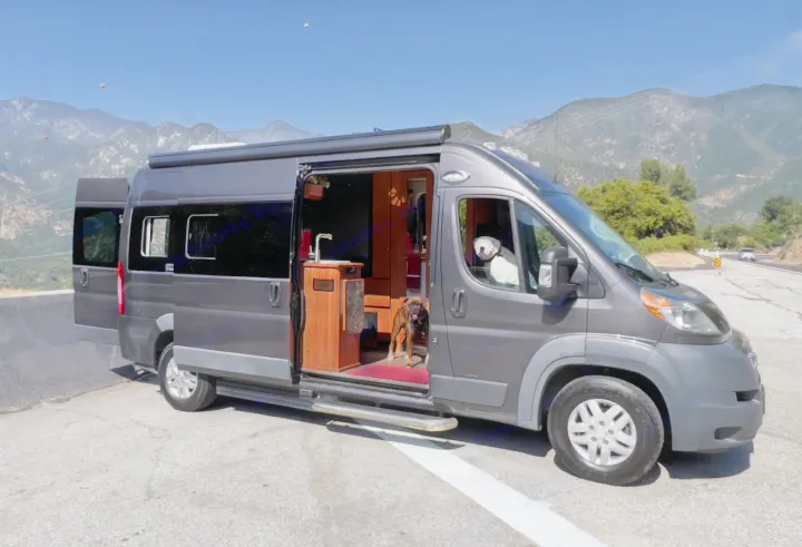 Gray RV rental parked by mountains, with its side & back doors open, revealing interior and two dogs.. Roadtrek Simplicity SRT 2019