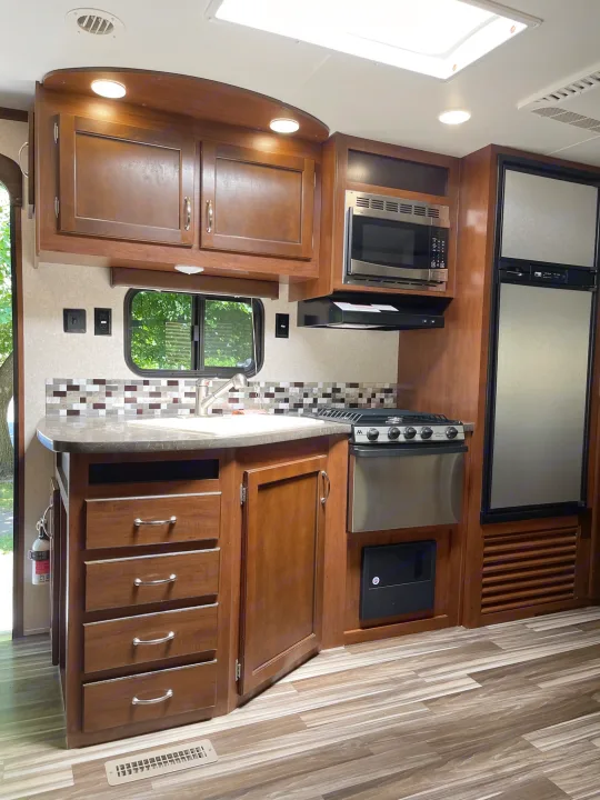 Modern RV rental kitchen with wood cabinets, microwave, stove, fridge, sink, and tiled backsplash for comfortable trips.. Jayco Jay Flight 2017