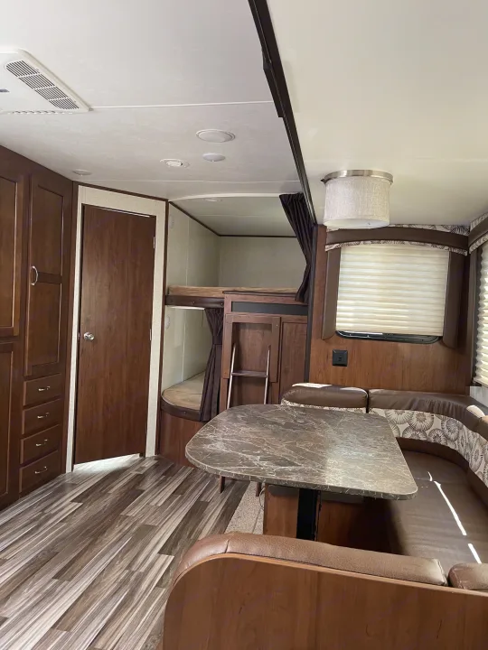 Inside an RV rental: view of the dinette with U-shaped seating, bunk beds, wood cabinetry, and laminate flooring.. Jayco Jay Flight 2017