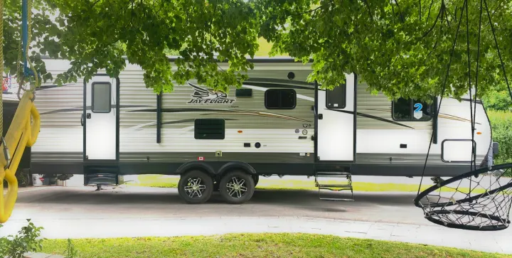 Jay Flight travel trailer, a spacious rv rental option, parked under lush trees with a swing set and net chair nearby.. Jayco Jay Flight 2017