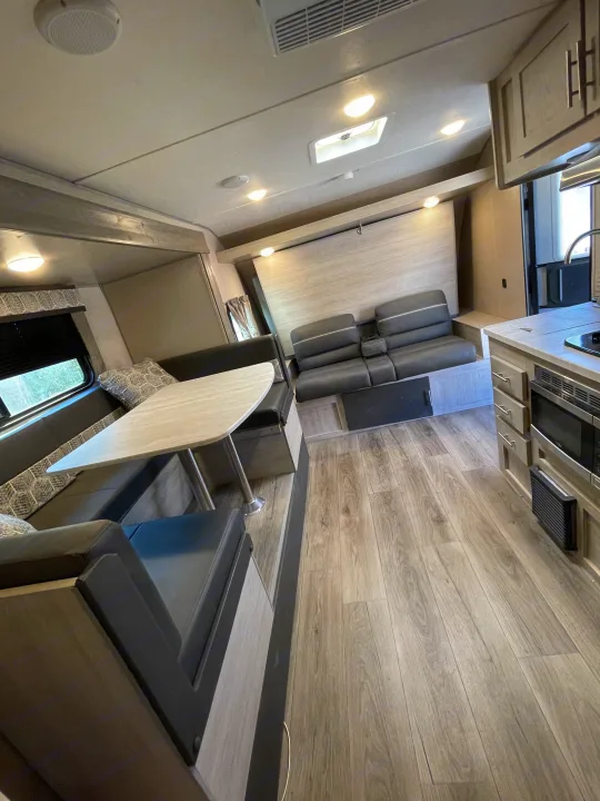 Clean & modern RV rental interior with a dinette, sofa, kitchen, and wood-look floors. Ready for adventures!. Coachmen Catalina Summit 2022
