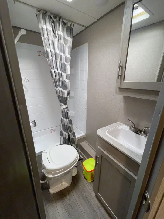 This RV rental bathroom features a compact shower, toilet, and sink vanity with a mirrored cabinet.. Coachmen Catalina Summit 2022