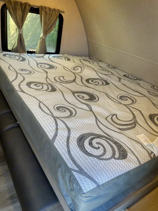 RV rental interior: cozy sleeping area with patterned mattress, window, and tie-back curtains.. Coachmen Catalina Summit 2022
