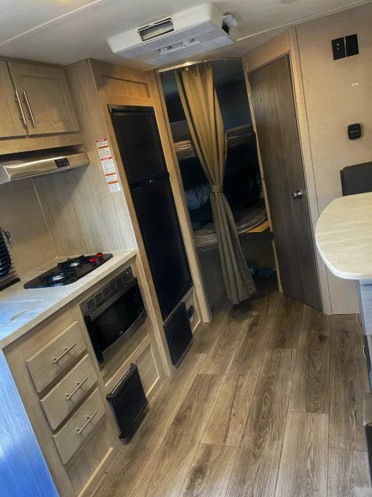 Compact RV rental interior featuring a full kitchen with stove, microwave, and fridge, plus cozy bunk beds.. Coachmen Catalina Summit 2022