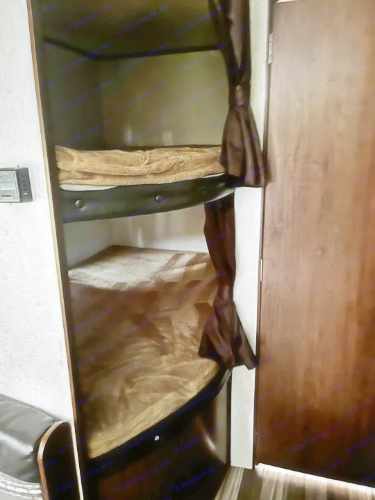 Interior view of an RV rental showing two stacked bunk beds with brown bedding and privacy curtains for a cozy sleep.. Jayco Jay Flight 2017