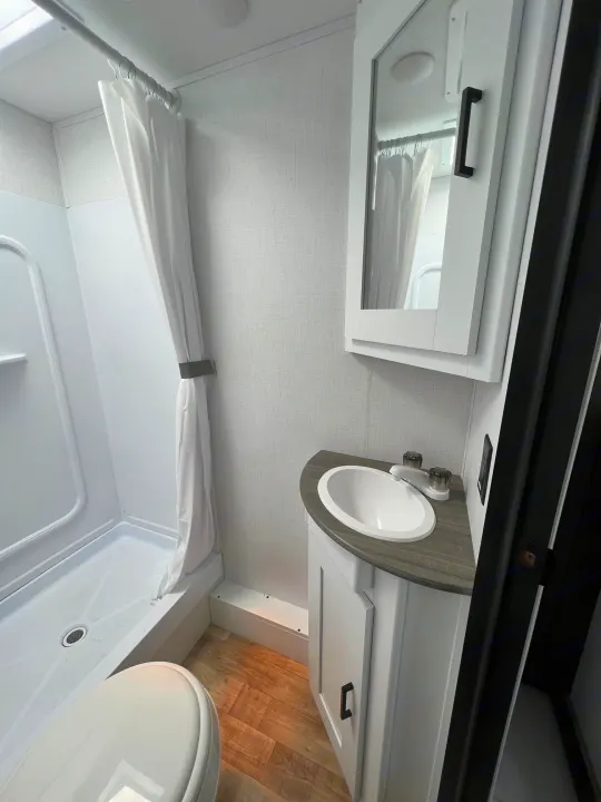 Clean RV rental bathroom featuring a sink, mirror, shower, and toilet.. Hideout 181BH 2023
