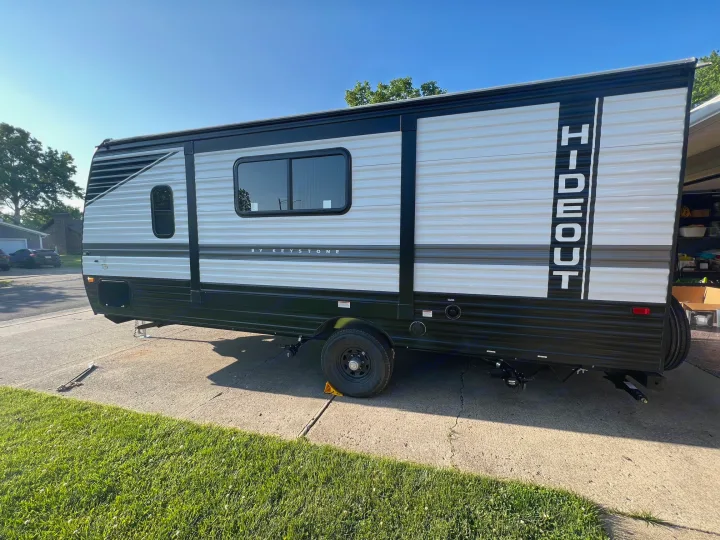 A sleek white and black Hideout travel trailer, ideal for an rv rental, is parked on a sunny driveway.. Hideout 181BH 2023