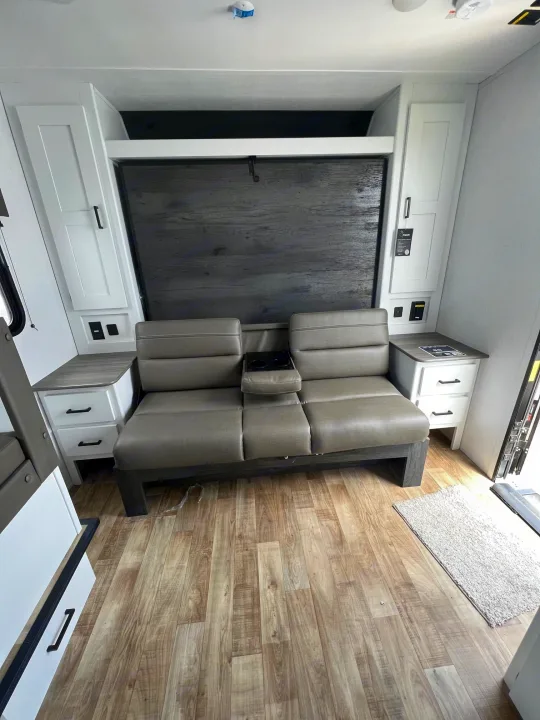 Inside an rv rental: a modern living area with cozy gray dinette seating, light wood flooring, and ample white storage cabinets.. Hideout 181BH 2023
