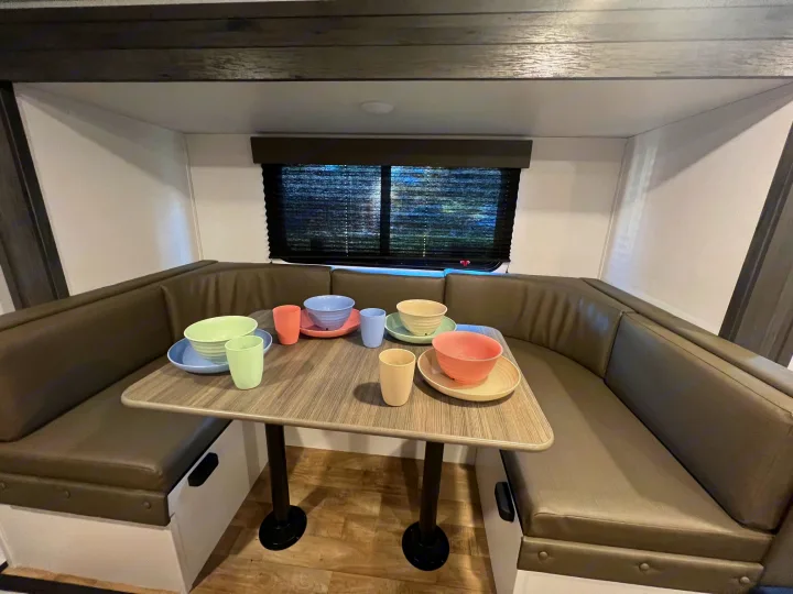 Inside an RV rental: a spacious dining booth with a table set with colorful dishes. Ideal for camper meals.. Hideout 181BH 2023