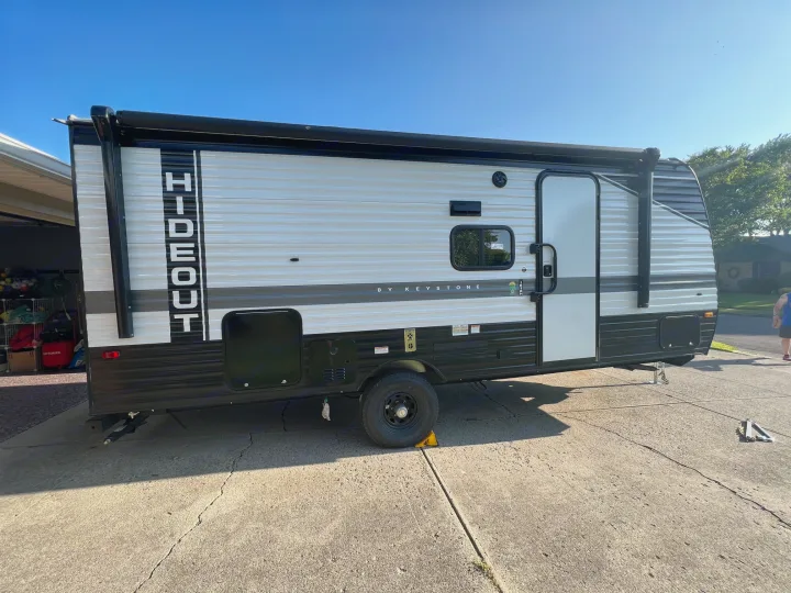 Modern 'Hideout by Keystone' travel trailer, white and black, parked on a sunny driveway. Perfect for your next RV rental adventure.. Hideout 181BH 2023