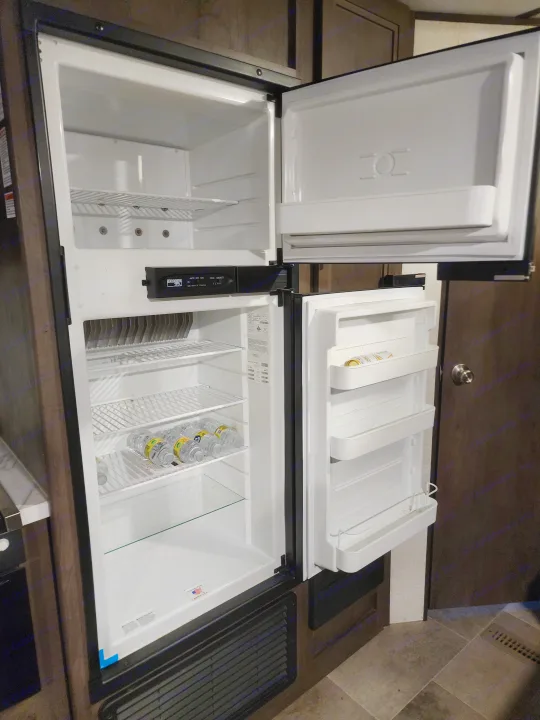 Top-loading RV rental refrigerator and freezer, open to reveal cold storage space with water bottles.. Coachmen lantern Dutchman 263 BHWE 2021