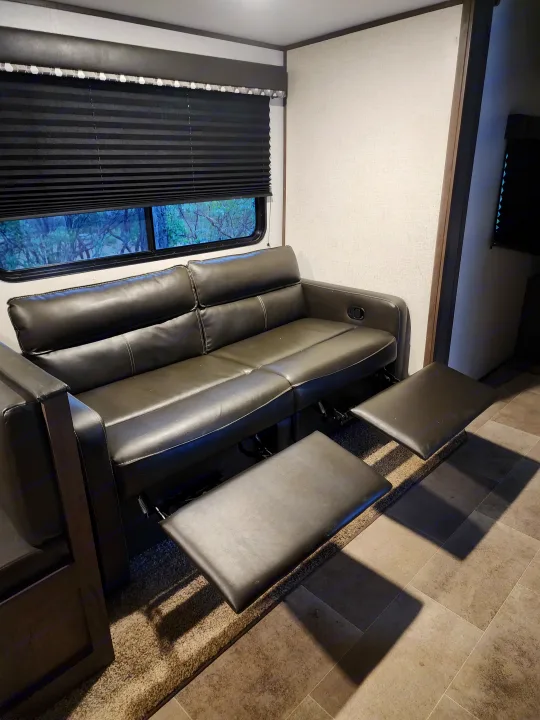 Spacious RV rental living area with comfortable reclining sofa, extended footrests, and window views. Ideal for relaxation.. Coachmen lantern Dutchman 263 BHWE 2021