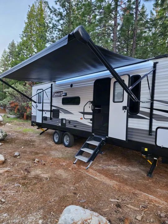 RV rental camping trip: a modern travel trailer with extended awning and steps in a natural setting.. Coachmen lantern Dutchman 263 BHWE 2021