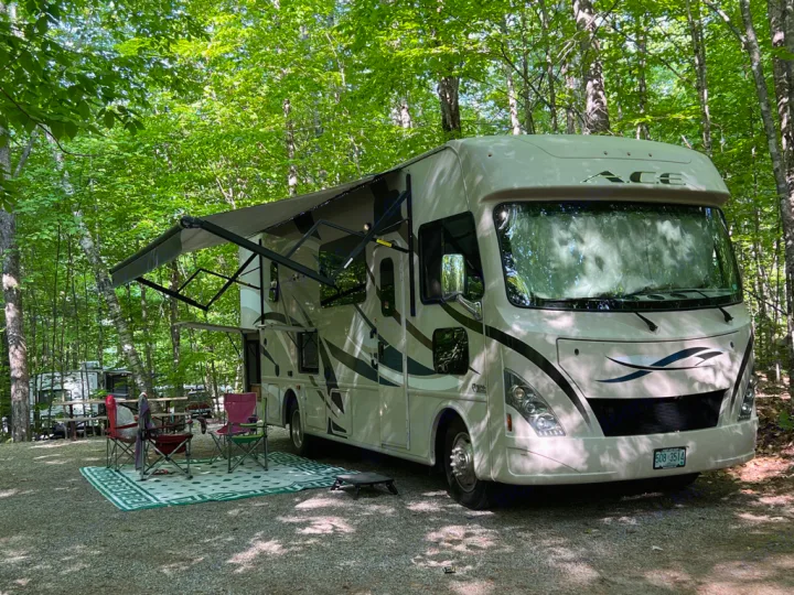 Enjoying an RV rental experience at a shaded campsite, complete with an extended awning and outdoor living space.. Thor Motor Coach A.C.E 2017