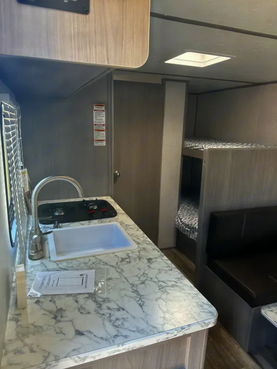 This compact rv rental interior features a functional kitchen with a sink and stovetop, bunk beds, and a cozy seating area.. Dutchmen Coleman Lantern LT 2022