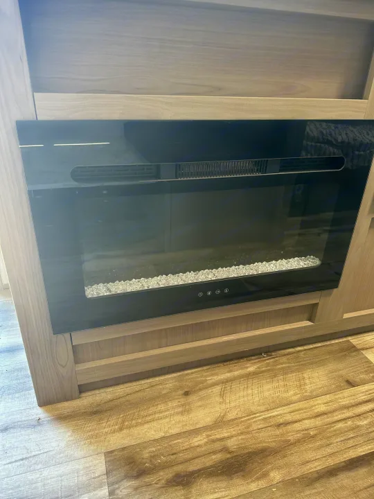 Modern electric fireplace in an RV rental, set in sleek wood cabinetry with crystal embers.. Dutchmen Coleman Lantern LT 2022