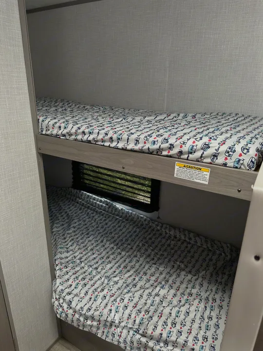 RV rental interior: bunk beds with playful camping sheets, a lower window, and a safety caution label on the upper bunk.. Dutchmen Coleman Lantern LT 2022