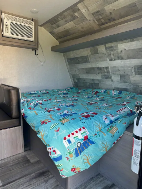 Inside an RV rental: a comfy bed with playful comforter, AC unit, and practical fire extinguisher.. Dutchmen Coleman Lantern LT 2022