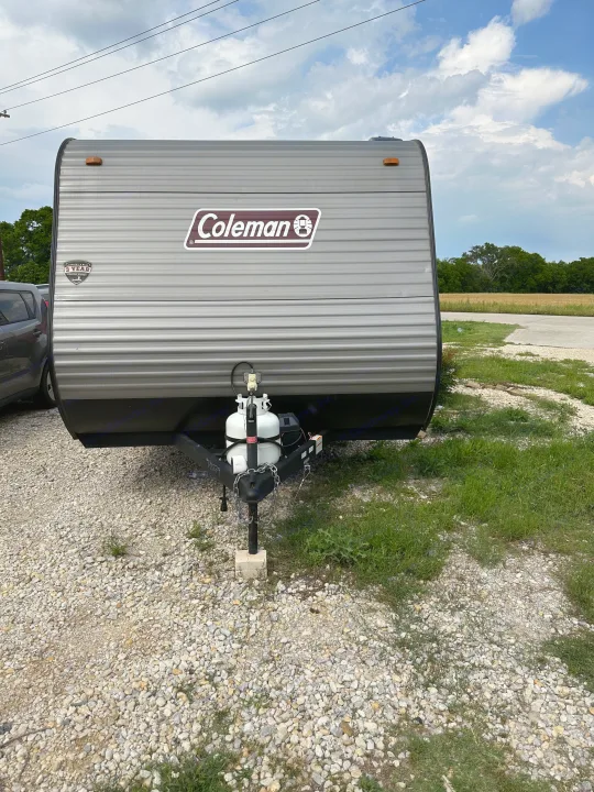 A gray Coleman travel trailer, an ideal rv rental, parked on gravel. Features front propane tanks for camping trips.. Dutchmen Coleman Lantern LT 2022