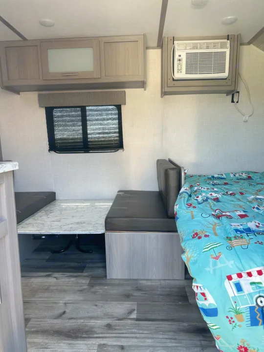 Inside an RV rental: a comfortable dinette converts to a bed, with wall-mounted AC and overhead storage.. Dutchmen Coleman Lantern LT 2022