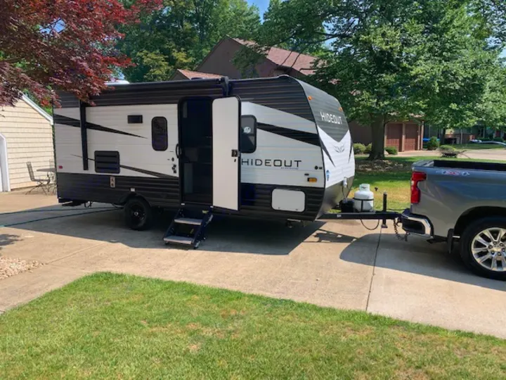 A gray pickup truck tows a white 'Hideout' RV rental trailer on a driveway, set for an adventure.. Keystone RV Hideout 2021