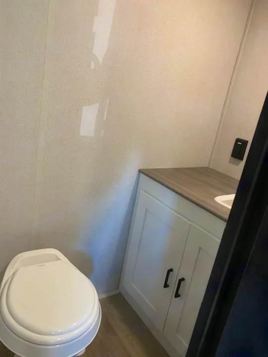 Inside an RV rental: a bright bathroom with a white toilet, light walls, and a stylish vanity cabinet.. Keystone RV Hideout 2021