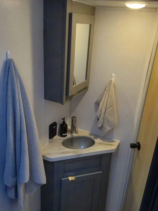 Modern rv rental bathroom vanity with a marble-look counter, circular sink, faucet, mirrored cabinet, and folded towels.. Ozark Ozark Trailer 2023