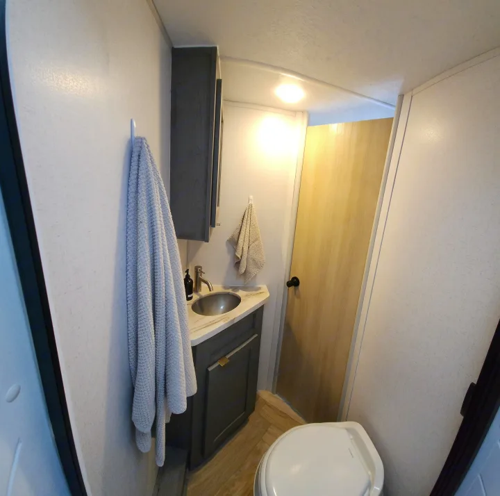Inside an RV rental, a compact bathroom with a sink, dark gray vanity, toilet, and textured light walls.. Ozark Ozark Trailer 2023