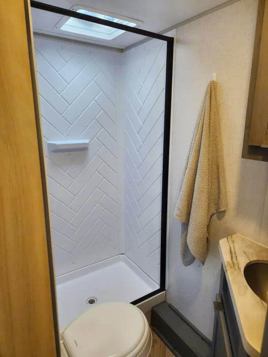 Bright RV rental bathroom: features a modern, herringbone-patterned shower, toilet, and vanity.. Ozark Ozark Trailer 2023