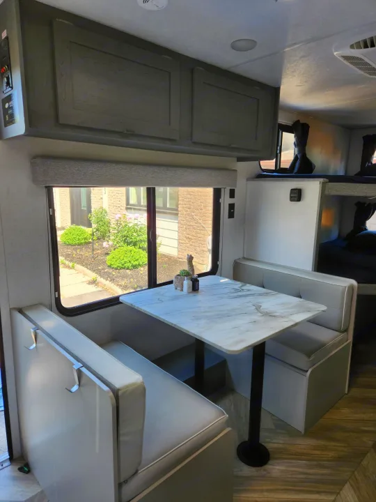 Spacious RV rental interior with a dinette, window view of greenery, and cozy bunk beds visible in the back.. Ozark Ozark Trailer 2023