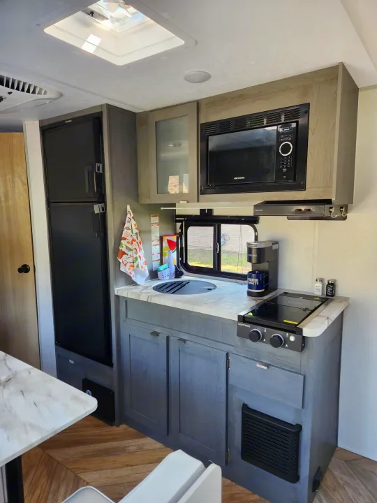 Overhead view of an RV rental kitchen showing a microwave, stove, sink, refrigerator drawers, and light-colored cabinetry.. Ozark Ozark Trailer 2023