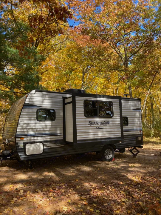 RV rental Springdale Mini in a colorful autumn campsite with fallen leaves under a blue sky.. Keystone RV Springdale 2019