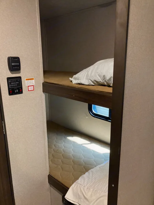 Cozy RV rental bunk beds seen from below. Features include a window, bedding, and a control panel for RV functions.. Keystone RV Springdale 2019