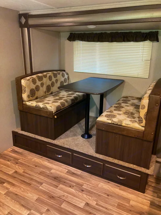 RV rental interior features a cozy dinette with patterned cushions, a table, and convenient storage for camper trips.. Keystone RV Springdale 2019