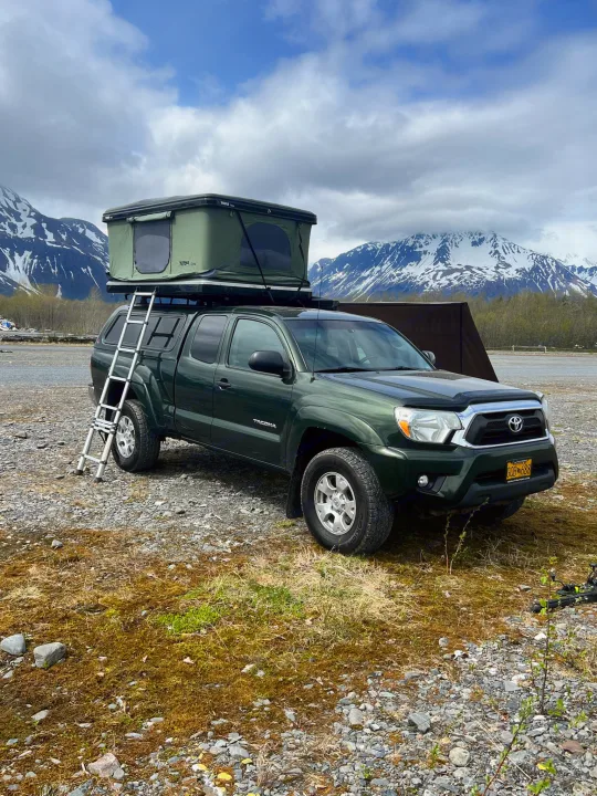 RV rental: A rugged Toyota Tacoma with a rooftop tent and ladder, set against snow-capped mountains, perfect for an outdoor adventure.. Toyota Tacoma 2012