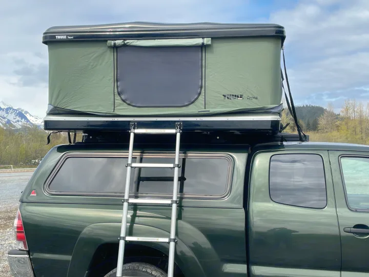 A green pickup truck with a ladder leading to a deployed Thule Tepui rooftop tent, ideal for RV rental camping.. Toyota Tacoma 2012