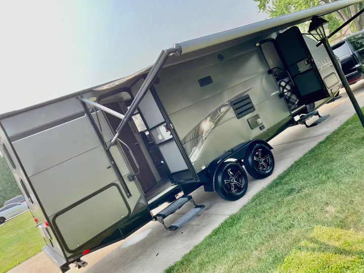 Sleek olive RV with extended awning and open door on pavement, ready for your next rv rental outdoor adventure.. Travel Lite Aura 2019