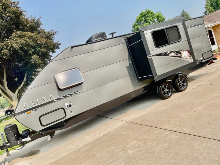 A sleek gray Aura travel trailer, with its side extended, parked on a sunny driveway. Perfect for an RV rental adventure.. Travel Lite Aura 2019