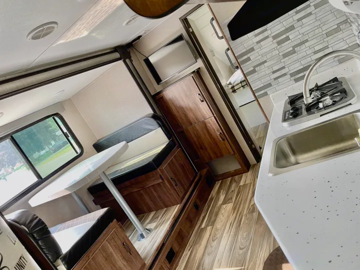 Inside an RV rental: kitchen with stove & sink, dinette, TV, and bedroom access. Modern, light interior.. Travel Lite Aura 2019