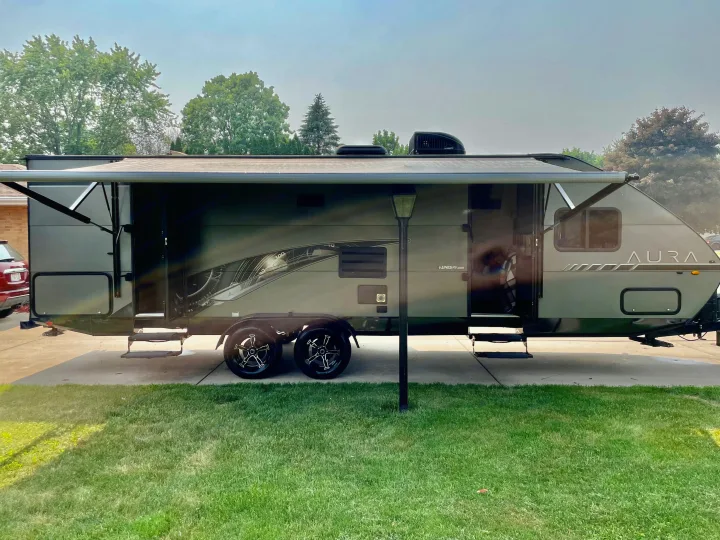 Spacious gray Aura travel trailer with extended awning, parked on a driveway. Great RV rental for your next trip.. Travel Lite Aura 2019